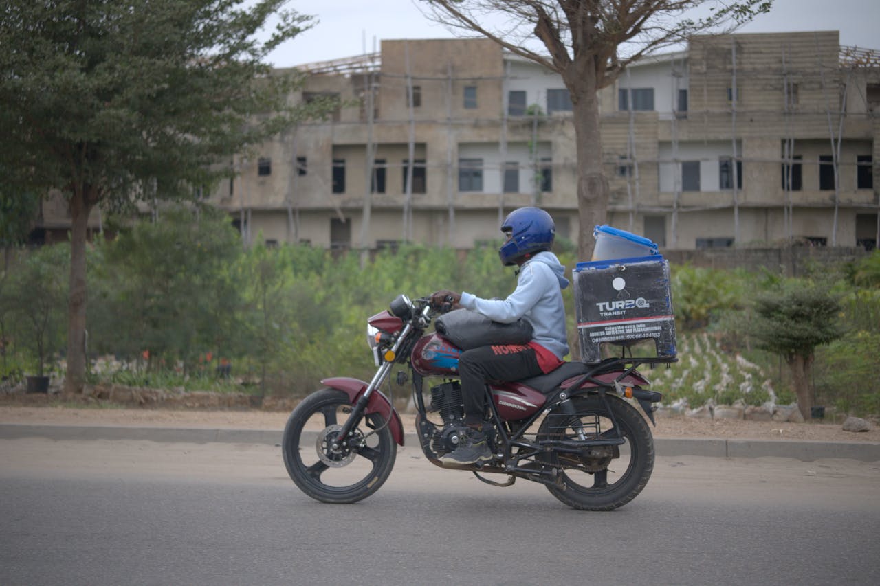 services-02 Motorcycle delivery rider with package box in urban Nigeria setting.
