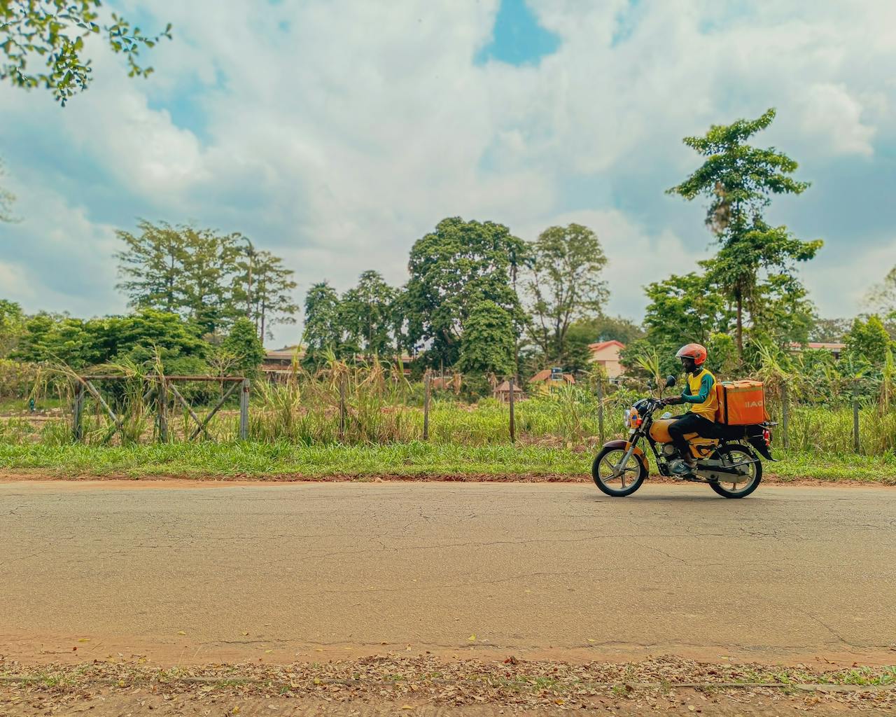 services-03 Motorbike courier riding along a rural road in Lagos, Nigeria. Vibrant and dynamic travel scene.