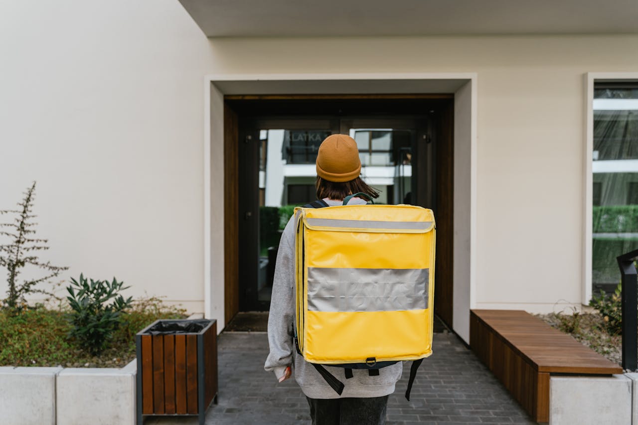 Mastering the First Impression: Your intriguing post title goes here A food delivery person with a yellow thermal backpack entering a modern building.